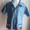 17.1 Chemise karabela tenue traditionnelle haïtienne de couleur bleue. Style ample. Deux poches latérales basses ornées chacune d'entre elles du drapeau Haïti. Cinq boutons non décoratifs centraux alignés de bas en haut de la chemise. Tissu 100% coton. Le col pouvant être surélevé selon le goût.