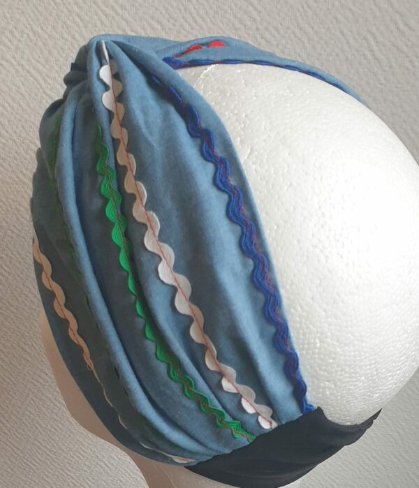 Bandeau féminin traditionnel haïtien sur fond bleu et agrémenté de guirlandes soigneusement colorées. Tissu noir et élastifié à l'arrière. Carabela. Taille unique. 27.95.jpg