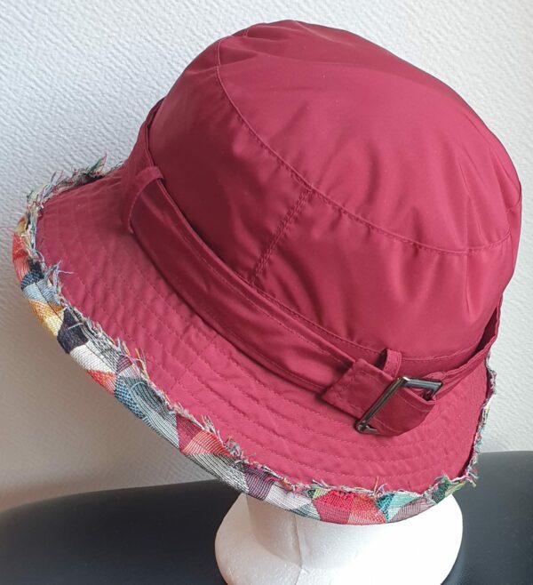 Bob unisexe de couleur rouge grenat imperméable et entièrement doublé en tissu polyester. Réglable à l'arrière par boucle de serrage. Finition biais en coton.