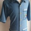 Chemise carabela traditionnelle haïtienne avec son col classique. Cinq boutons en bois sont disposés sur le devant en ligne centrale. Trois poches brodées à la main avec sur la poche droite une petite maison traditionnelle ancestrale. Une poche miniaturisée se distingue sur la demie manche gauche.