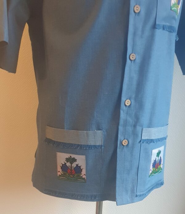 Chemise carabela en tissu cent pour cent coton. Trois poches munies du drapeau haïtien. Tissu travaillé à la main avec une petite poche confectionnée sur la manche gauche. Un Col classique a été choisi pour ce modèle avec un ensemble de boutons en bois coco verticaux. Made in Paris.