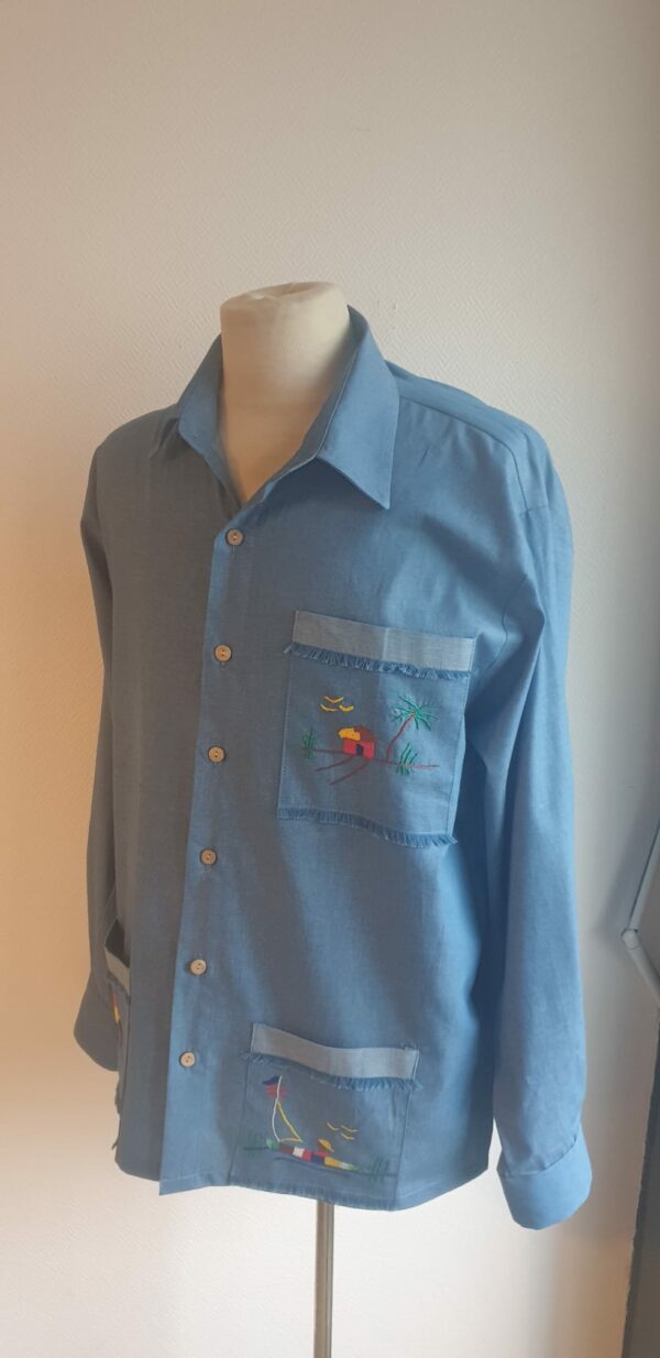 Chemise carabela traditionnelle haïtienne de couleur bleue confectionnée en France. Trois poches brodées main. Ensemble de boutons verticaux et centraux en bois coco. Tissu cent pour cent coton. Création artisanale Anjero