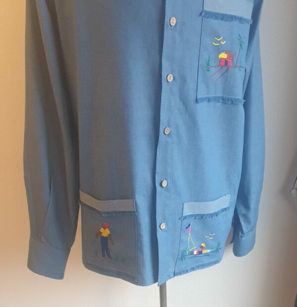 Chemise carabela traditionnelle haïtienne de couleur bleue confectionnée en France. Trois poches brodées main. Ensemble de boutons verticaux et centraux en bois coco. Tissu cent pour cent coton. Création artisanale Anjero