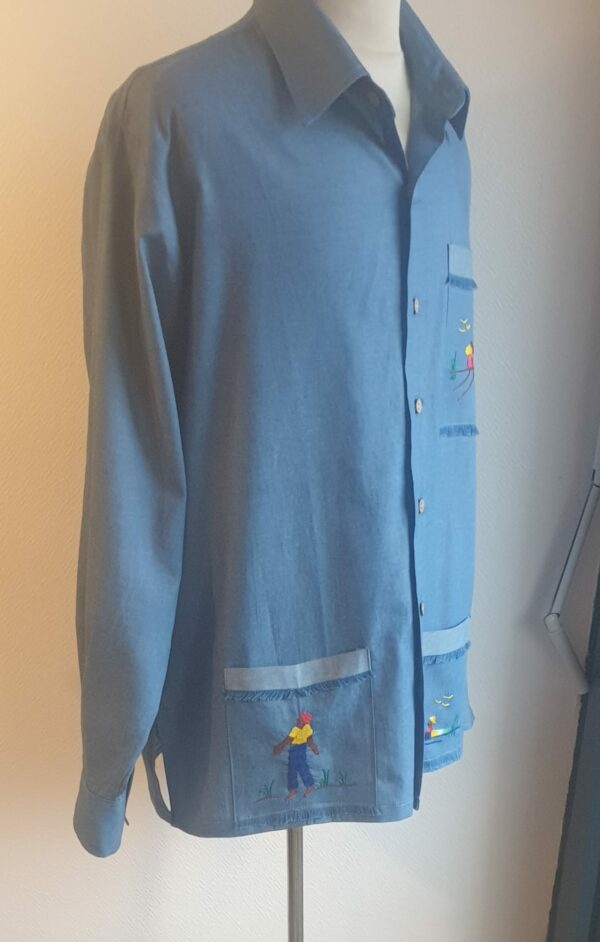 Chemise carabela traditionnelle haïtienne de couleur bleue confectionnée en France. Trois poches brodées main. Ensemble de boutons verticaux et centraux en bois coco. Tissu cent pour cent coton. Création artisanale Anjero