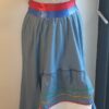 Robe Carabela cintrée sur fond bleu et sur une tenue traditionnelle haïtienne pour cérémonie, mariage, gala, baptême. Une finition au col de la robe et sur son bas de jupe est brodé en dentelles anglaises. Un jupon blanc garni de dentelles soigneusement confectionnées dans la robe, des serpentines aux quadruples couleurs jaune, bleu, blanc, rouge; Une grande ceinture aux couleurs du drapeau haïtien; Un tissu cent pour cent coton; Une souplesse à la taille à laquelle est intégré un élastique sont autant de particularités qui confèrent à la confection une entière originalité. Made in Paris. Créé par Anjero.