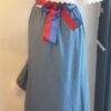 Robe Carabela cintrée sur fond bleu et sur une tenue traditionnelle haïtienne pour cérémonie, mariage, gala, baptême. Une finition au col de la robe et sur son bas de jupe est brodé en dentelles anglaises. Un jupon blanc garni de dentelles soigneusement confectionnées dans la robe, des serpentines aux quadruples couleurs jaune, bleu, blanc, rouge; Une grande ceinture aux couleurs du drapeau haïtien; Un tissu cent pour cent coton; Une souplesse à la taille à laquelle est intégré un élastique sont autant de particularités qui confèrent à la confection une entière originalité. Made in Paris. Créé par Anjero.