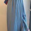 Robe Carabela cintrée sur fond bleu et sur une tenue traditionnelle haïtienne pour cérémonie, mariage, gala, baptême. Une finition au col de la robe et sur son bas de jupe est brodé en dentelles anglaises. Un jupon blanc garni de dentelles soigneusement confectionnées dans la robe, des serpentines aux quadruples couleurs jaune, bleu, blanc, rouge; Une grande ceinture aux couleurs du drapeau haïtien; Un tissu cent pour cent coton; Une souplesse à la taille à laquelle est intégré un élastique sont autant de particularités qui confèrent à la confection une entière originalité. Made in Paris. Créé par Anjero.