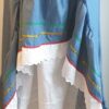 Robe Carabela cintrée sur fond bleu et sur une tenue traditionnelle haïtienne pour cérémonie, mariage, gala, baptême. Une finition au col de la robe et sur son bas de jupe est brodé en dentelles anglaises. Un jupon blanc garni de dentelles soigneusement confectionnées dans la robe, des serpentines aux quadruples couleurs jaune, bleu, blanc, rouge; Une grande ceinture aux couleurs du drapeau haïtien; Un tissu cent pour cent coton; Une souplesse à la taille à laquelle est intégré un élastique sont autant de particularités qui confèrent à la confection une entière originalité. Made in Paris. Créé par Anjero.