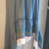 Robe Carabela cintrée sur fond bleu et sur une tenue traditionnelle haïtienne pour cérémonie, mariage, gala, baptême. Une finition au col de la robe et sur son bas de jupe est brodé en dentelles anglaises. Un jupon blanc garni de dentelles soigneusement confectionnées dans la robe, des serpentines aux quadruples couleurs jaune, bleu, blanc, rouge; Une grande ceinture aux couleurs du drapeau haïtien; Un tissu cent pour cent coton; Une souplesse à la taille à laquelle est intégré un élastique sont autant de particularités qui confèrent à la confection une entière originalité. Made in Paris. Créé par Anjero.