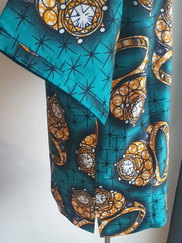 8.4Chemise en tissu coton wax assortie d'un imprimé bague or sur fond vert bleu océan. Ce modèle est conçu en manches courtes. Une fermeture éclaire à bout fermé subtilement dissimulée est ajoutée sur l'épaule gauche. Elle est faite de nylon souple et d'une tête de fermeture à glissière en métal, solide et durable. La dent de la fermeture à glissière est lisse et ne s'accroche pas, ajoutant ainsi, une touche attractive et supplémentaire à la confection. Taille unique. Ce produit est entièrement confectionné en atelier, en série limitée, par AnjeroCréation.