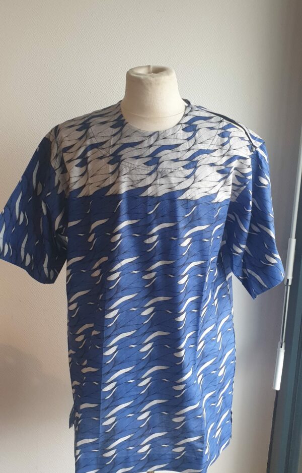 9.1Chemise en tissu coton wax assortie d'un imprimé en vagues océaniques sur fond bleu et inversé sur fond blanc. Ce modèle est conçu en manches courtes. Une fermeture éclaire à bout fermé subtilement dissimulée est ajoutée sur l'épaule gauche. Elle est faite de nylon souple et d'une tête de fermeture à glissière en métal, solide et durable. La dent de la fermeture à glissière est lisse et ne s'accroche pas, ajoutant ainsi, une touche attractive et supplémentaire à la confection. Taille unique. Ce produit est entièrement confectionné, en série limitée, par Anjero. Prix : 39,95€.