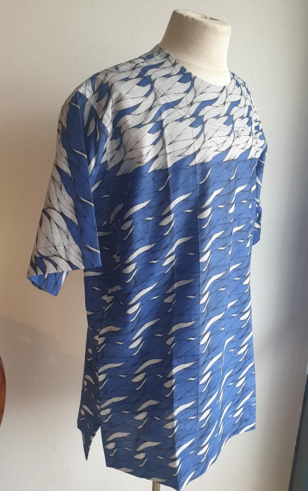 9.2Chemise en tissu coton wax assortie d'un imprimé montrant des formes de vagues océaniques sur fond bleu et inversé sur fond blanc. Ce modèle est conçu en manches courtes. Une fermeture éclaire à bout fermé subtilement dissimulée est ajoutée sur l'épaule gauche. Elle est faite de nylon souple et d'une tête de fermeture à glissière en métal, solide et durable. La dent de la fermeture à glissière est lisse et ne s'accroche pas, ajoutant ainsi, une touche attractive et supplémentaire à la confection. Taille unique. Ce produit est entièrement confectionné en atelier, en série limitée, par AnjeroCréation.