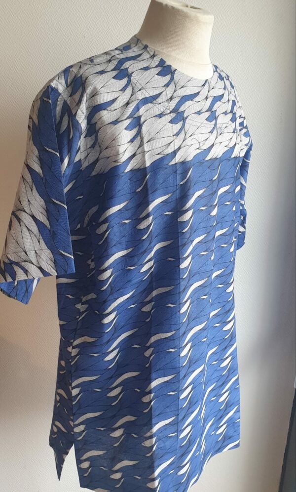 9.3Chemise en tissu coton wax assortie d'un imprimé montrant des formes de vagues océaniques sur fond bleu et inversé sur fond blanc. Ce modèle est conçu en manches courtes. Une fermeture éclaire à bout fermé subtilement dissimulée est ajoutée sur l'épaule gauche. Elle est faite de nylon souple et d'une tête de fermeture à glissière en métal, solide et durable. La dent de la fermeture à glissière est lisse et ne s'accroche pas, ajoutant ainsi, une touche attractive et supplémentaire à la confection. Taille unique. Ce produit est entièrement confectionné en atelier, en série limitée, par AnjeroCréation.