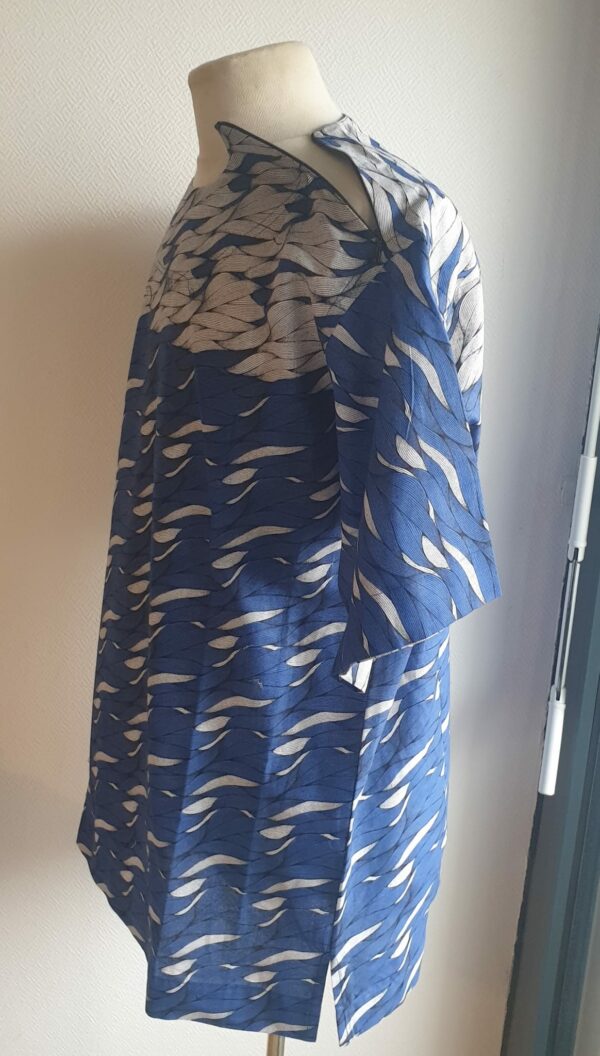 9.4Chemise en tissu coton wax assortie d'un imprimé montrant des formes de vagues océaniques sur fond bleu et inversé sur fond blanc. Ce modèle est conçu en manches courtes. Une fermeture éclaire à bout fermé subtilement dissimulée est ajoutée sur l'épaule gauche. Elle est faite de nylon souple et d'une tête de fermeture à glissière en métal, solide et durable. La dent de la fermeture à glissière est lisse et ne s'accroche pas, ajoutant ainsi, une touche attractive et supplémentaire à la confection. Taille unique. Ce produit est entièrement confectionné en atelier, en série limitée, par AnjeroCréation.