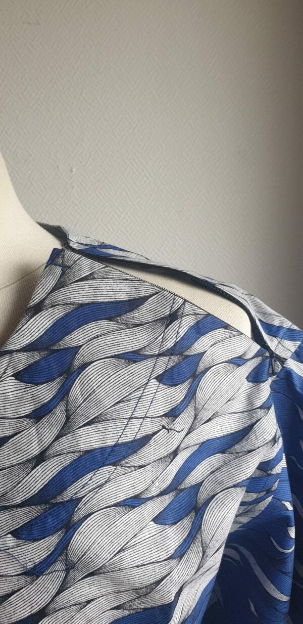 9.5Chemise en tissu coton wax assortie d'un imprimé montrant des formes de vagues océaniques sur fond bleu et inversé sur fond blanc. Ce modèle est conçu en manches courtes. Une fermeture éclaire à bout fermé subtilement dissimulée est ajoutée sur l'épaule gauche. Elle est faite de nylon souple et d'une tête de fermeture à glissière en métal, solide et durable. La dent de la fermeture à glissière est lisse et ne s'accroche pas, ajoutant ainsi, une touche attractive et supplémentaire à la confection. Taille unique. Ce produit est entièrement confectionné en atelier, en série limitée, par AnjeroCréation.