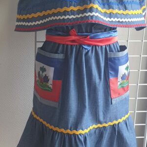 2.1Robe enfant carabela sur une tenue traditionnelle haïtienne. Un ruban élastique à la taille est intégré avec le placement de deux jolies poches l'une comme l'autre décorées avec le drapeau haïtien. Une ceinture bicolore est mise en évidence et singularise ce vêtement dont l'aisance et la douceur qui seront une révélation au porté, ne laisseront pas de vous surprendre. Taille : 6 et 7 ans. Prix : 109.95€. Cette confection est réalisée à Paris et est signée par le maître tailleur AnjeroCréation. 