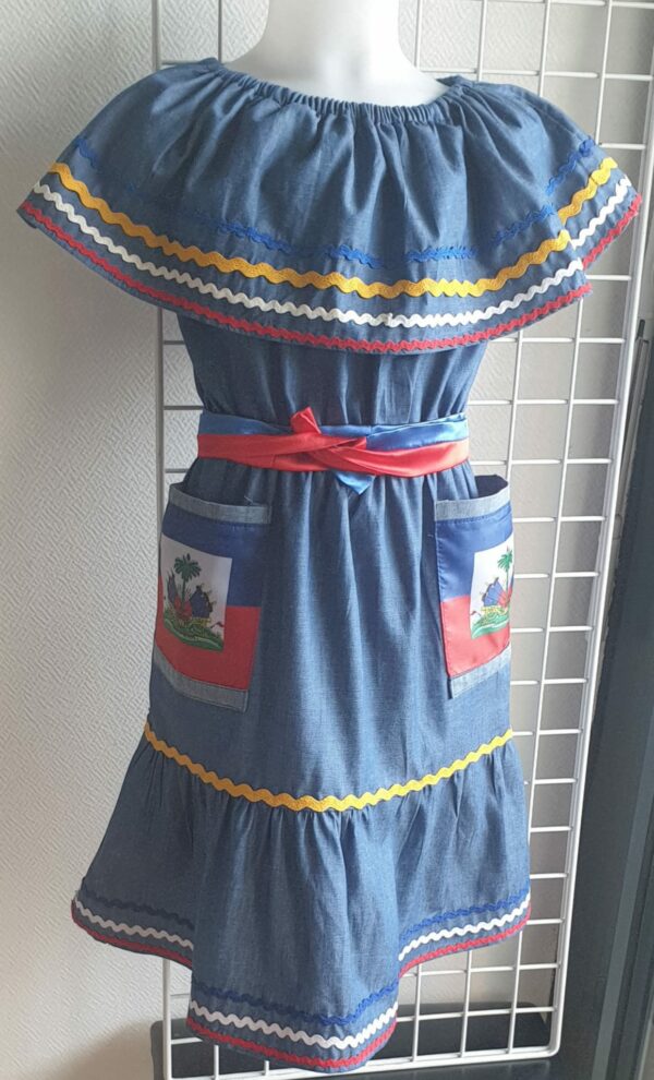 2.4Robe enfant carabela sur une tenue traditionnelle haïtienne. Un ruban élastique à la taille est intégré avec le placement de deux jolies poches l'une comme l'autre décorées avec le drapeau haïtien. Une ceinture bicolore est mise en évidence et singularise ce vêtement dont l'aisance et la douceur qui seront une révélation au porté, ne laisseront pas de vous surprendre. Cette confection est réalisée à Paris et est signée par le maître tailleur AnjeroCréation.