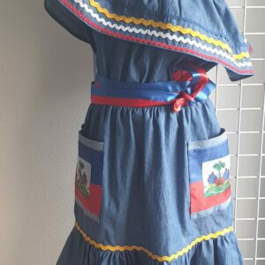 3.1Robe enfant carabela sur une tenue traditionnelle haïtienne. Un ruban élastique à la taille est intégré avec le placement de deux jolies poches l'une comme l'autre décorées avec le drapeau haïtien. Une ceinture bicolore est mise en évidence et singularise ce vêtement dont l'aisance et la douceur qui seront une révélation au porté, ne laisseront pas de vous surprendre. Taille : 9 et 10 ans. Prix : 125.95€. Cette confection est réalisée à Paris et est signée par le maître tailleur AnjeroCréation. 