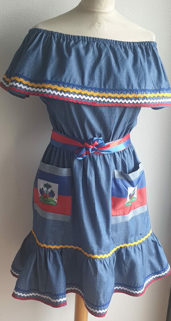 3.3Robe enfant carabela sur une tenue traditionnelle haïtienne. Un ruban élastique à la taille est intégré avec le placement de deux jolies poches l'une comme l'autre décorées avec le drapeau haïtien. Une ceinture bicolore est mise en évidence et singularise ce vêtement dont l'aisance et la douceur qui seront une révélation au porté, ne laisseront pas de vous surprendre. Cette confection est réalisée à Paris et est signée par le maître tailleur AnjeroCréation. 