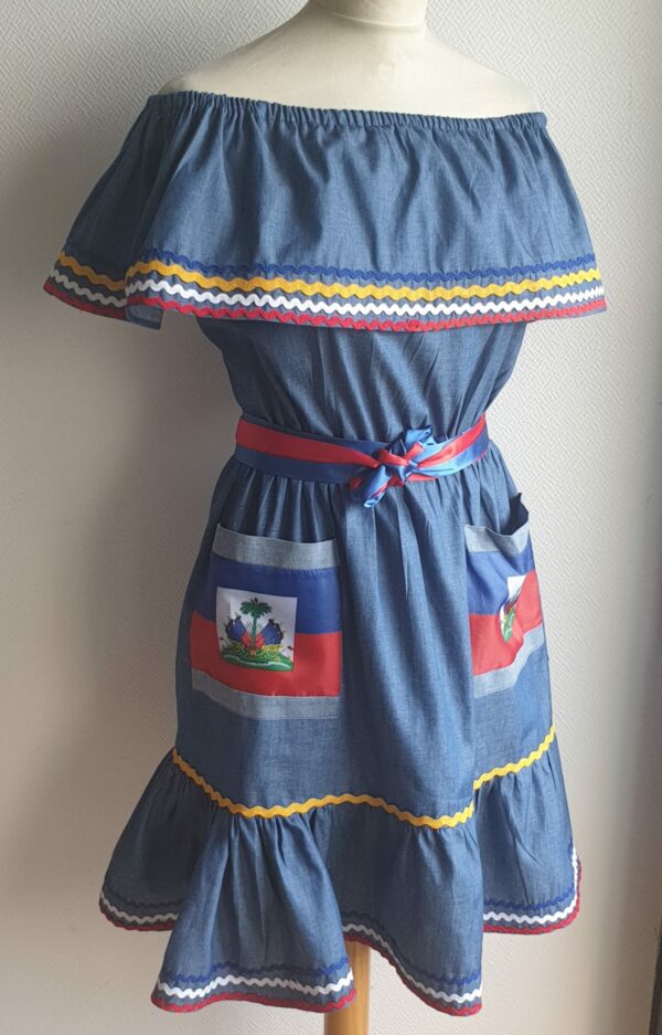 3.4Robe enfant carabela sur une tenue traditionnelle haïtienne. Un ruban élastique à la taille est intégré avec le placement de deux jolies poches l'une comme l'autre décorées avec le drapeau haïtien. Une ceinture bicolore est mise en évidence et singularise ce vêtement dont l'aisance et la douceur qui seront une révélation au porté, ne laisseront pas de vous surprendre. Cette confection est réalisée à Paris et est signée par le maître tailleur AnjeroCréation. 