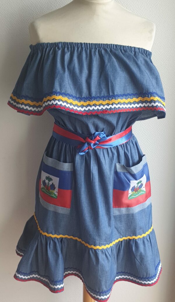 4.2Robe enfant carabela sur une tenue traditionnelle haïtienne. Ce vêtement est élastique à la taille. Il est présenté avec ses deux poches ornées du draapeau d'Haïti et sa ceinture bicolore en rouge et bleue. Entièrement conçu et réalisé aux ateliers AnjeroCréation à Paris.