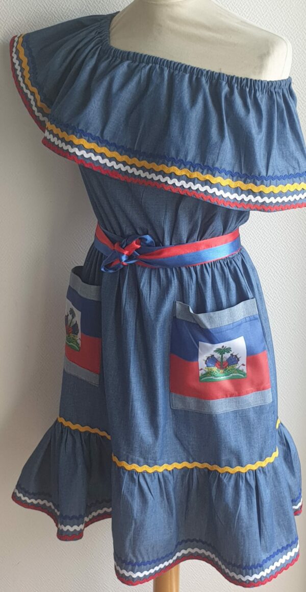 4.4Robe enfant carabela sur une tenue traditionnelle haïtienne. Ce vêtement est élastique à la taille. Il est présenté avec ses deux poches ornées du draapeau d'Haïti et sa ceinture bicolore en rouge et bleue. Taille : 6, 7 ans. Entièrement conçu et réalisé aux ateliers AnjeroCréation à Paris.
