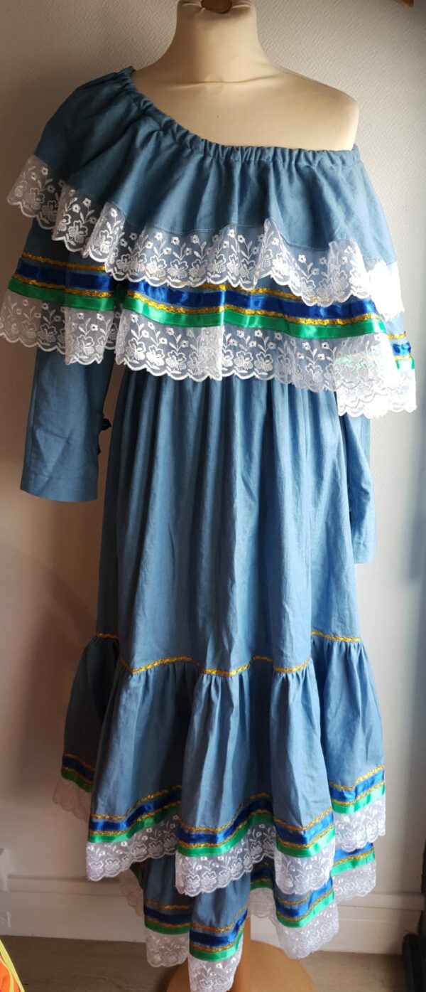 6.1robe carabela pour cérémonie, mariage, baptême, gala sur une tenue traditionnelle haïtienne en bleu. C'est une robe longue sur deux étages avec deux cols bardots superposés. Les bas de la robe et des cols sont garnis de zigzags couleur or, de rubans bleus royals et verts. Le jupon est soigneusement intégré à la robe. Les manches sont longues et en fentes munies de trois petits boutons. Cette confection douce à porter est élastique à la taille et livrée avec une ceinture formant un ensemble harmonieux. Un grand et soyeux foulard en tour de tête est également proposé dimentionné à 1,50m sur 0,32m. Taille : S, M, L, XL. Entièrement conçu et réalisé par les ateliers AnjeroCréation à Paris. Prix : 549.95€