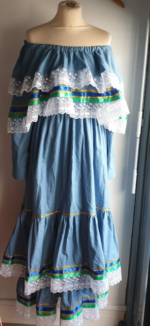 6.2robe carabela pour cérémonie, mariage, baptême, gala sur une tenue traditionnelle haïtienne en bleu. C'est une robe longue sur deux étages avec deux cols bardots superposés. Les bas de la robe et des cols sont garnis de zigzags couleur or, de rubans bleus royals et verts. Le jupon est soigneusement intégré à la robe. Les manches sont longues et en fentes munies de trois petits boutons. Cette confection douce à porter est élastique à la taille et livrée avec une ceinture formant un ensemble harmonieux. Un grand et soyeux foulard en tour de tête est également proposé dimentionné à 1,50m sur 0,32m. Entièrement conçu et réalisé par les ateliers AnjeroCréation à Paris.