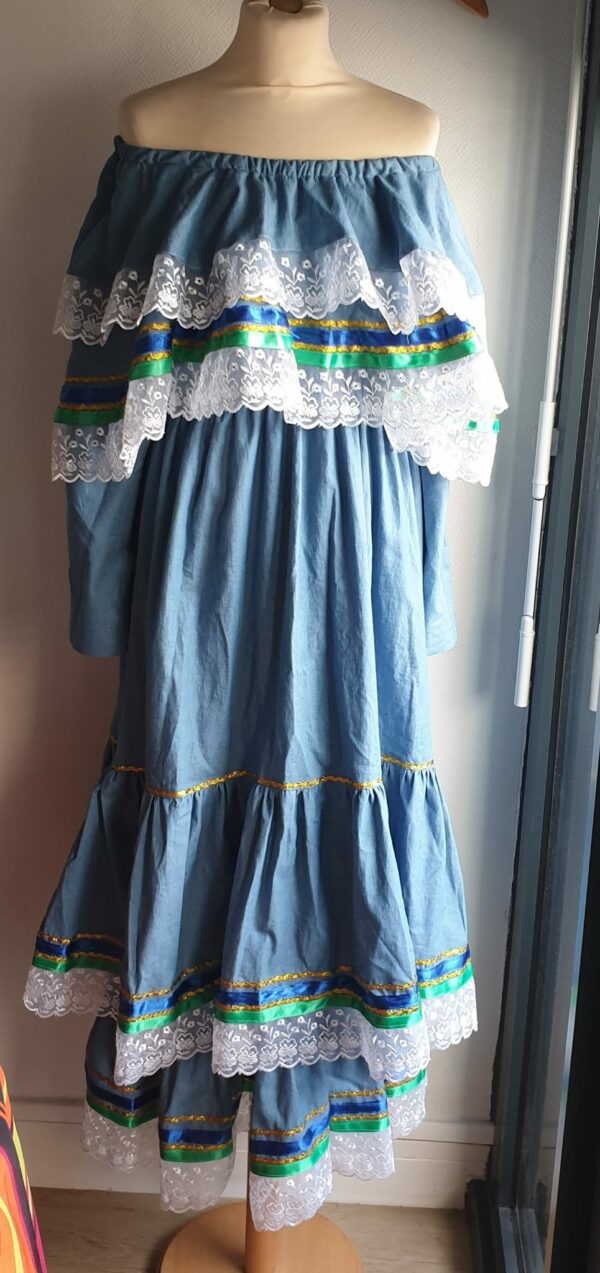 6.3robe carabela pour cérémonie, mariage, baptême, gala sur une tenue traditionnelle haïtienne en bleu. C'est une robe longue sur deux étages avec deux cols bardots superposés. Les bas de la robe et des cols sont garnis de zigzags couleur or, de rubans bleus royals et verts. Le jupon est soigneusement intégré à la robe. Les manches sont longues et en fentes munies de trois petits boutons. Cette confection douce à porter est élastique à la taille et livrée avec une ceinture formant un ensemble harmonieux. Un grand et soyeux foulard en tour de tête est également proposé dimentionné à 1,50m sur 0,32m. Entièrement conçu et réalisé par les ateliers AnjeroCréation.