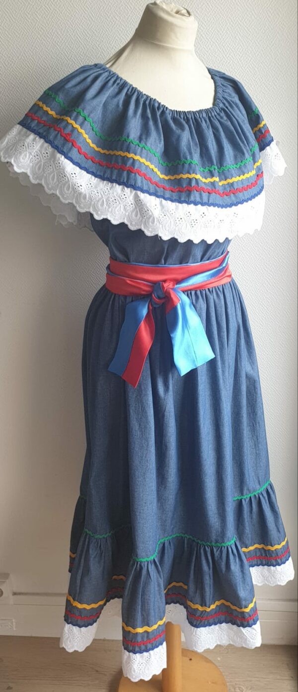 8.2Robe carabela en bleu sur une tenue traditionnelle haïtienne. Très large et élastique à la taille. Zigzag et diversité de couleurs. Dentelle broderie sur le haut ett le bas de la robe. L'ajout d'une ceinture bicolore rouge bleue apporte une touche harmonieuse à la confection. Taille : S, M, L, XL, XXL. Entièrement conçue et réalisée aux ateliers AnjeroCréation à Paris.