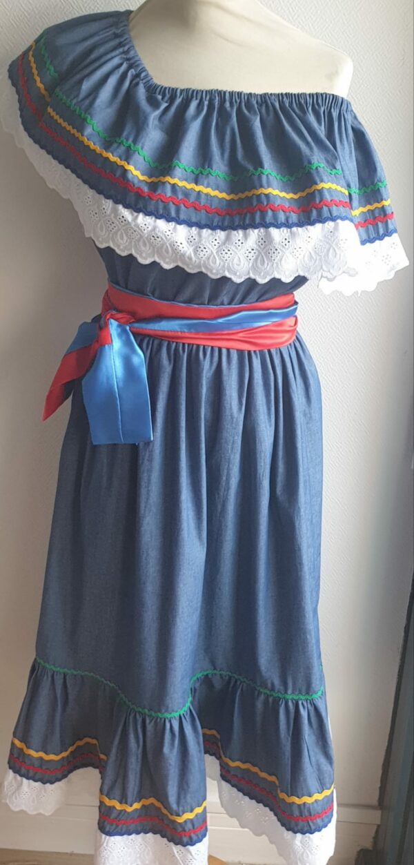 8.4Robe carabela en bleu sur une tenue traditionnelle haïtienne. Très large et élastique à la taille. Zigzag et diversité de couleurs. Dentelle broderie sur le haut ett le bas de la robe. L'ajout d'une ceinture bicolore rouge bleue apporte une touche harmonieuse à la confection. Taille : S, M, L, XL, XXL. Entièrement conçue et réalisée aux ateliers AnjeroCréation à Paris.