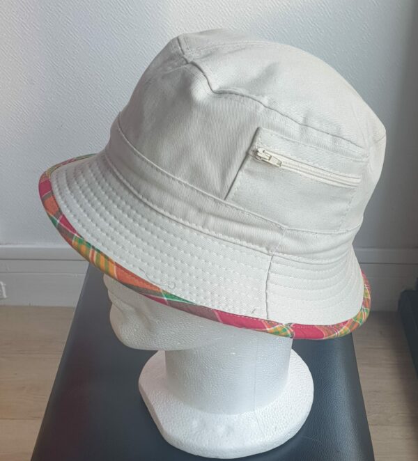 10.2Bob en blanc cassé sur un tissu 100% coton. L'ajout de deux poches latérales zipées apporte une touche harmonieuse à ce couvre-chef. Les finitions en bordure sont en Madras et entièrement conçues puis réalisées aux ateliers AnjeroCréation.