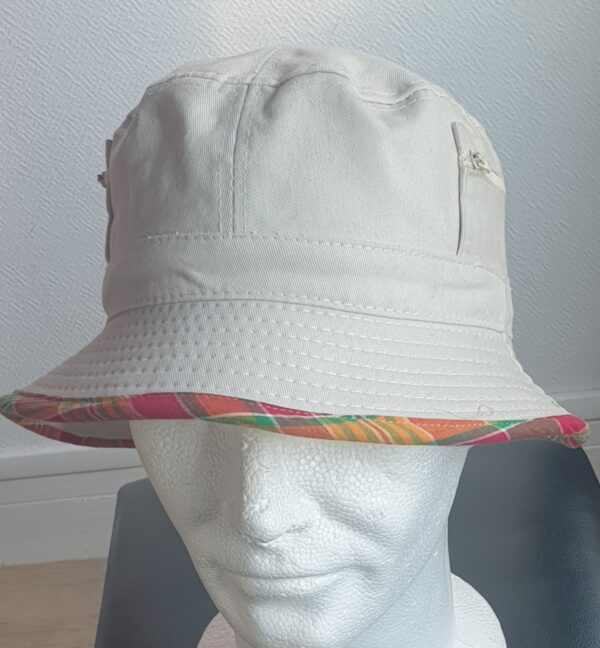 10.1Bob en blanc cassé sur un tissu 100% coton. L'ajout de deux poches latérales zipées apporte une touche harmonieuse à ce couvre-chef. Les finitions en bordure sont en Madras et entièrement conçues puis réalisées aux ateliers AnjeroCréation à Paris.