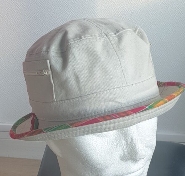 10.3Bob en blanc cassé sur un tissu 100% coton. L'ajout de deux poches latérales zipées apporte une touche harmonieuse à ce couvre-chef. Les finitions en bordure sont en Madras et entièrement conçues puis réalisées aux ateliers AnjeroCréation.