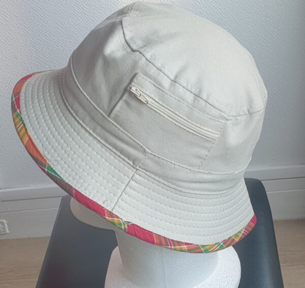 10.4Bob en blanc cassé sur un tissu 100% coton. L'ajout de deux poches latérales zipées apporte une touche harmonieuse à ce couvre-chef. Les finitions en bordure sont en Madras et entièrement conçues puis réalisées aux ateliers AnjeroCréation.