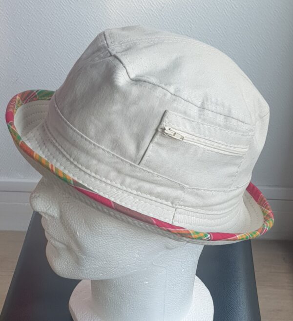 10.5Bob en blanc cassé sur un tissu 100% coton. L'ajout de deux poches latérales zipées apporte une touche harmonieuse à ce couvre-chef. Les finitions en bordure sont en Madras et entièrement conçues puis réalisées aux ateliers AnjeroCréation.