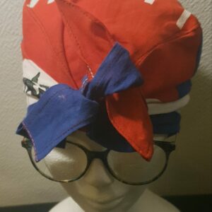 2.1Turban pleine tête orné du drapeau haïtien. Ce couvre-chef apparenté tout à fait original dispose d'une parfaite élasticité à l'arrière pour une adaptation idéale. Ce dernier est conçu et réalisé aux ateliers AnjeroCréation  à Paris. Prix : 23.50€.