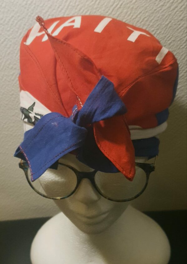 2.1Turban pleine tête orné du drapeau haïtien. Ce couvre-chef apparenté tout à fait original dispose d'une parfaite élasticité à l'arrière pour une adaptation idéale. Ce dernier est conçu et réalisé aux ateliers AnjeroCréation  à Paris. Prix : 23.50€.