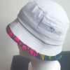 2.3Bob tout en blanc sur un tissu 100% coton. L'ajout de deux poches latérales zipées apporte une touche harmonieuse à la confection. Les finitions en bordure sur le pourtour de ce couvre-chef sont en WAX et réalisées aux ateliers AnjeroCréation.