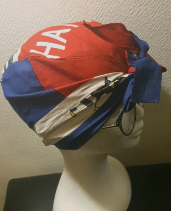2.4Turban pleine tête orné du drapeau haïtien. Ce couvre-chef apparenté tout à fait original dispose d'une parfaite élasticité à l'arrière pour une adaptation idéale. Ce dernier est conçu et réalisé aux ateliers AnjeroCréation  à Paris.