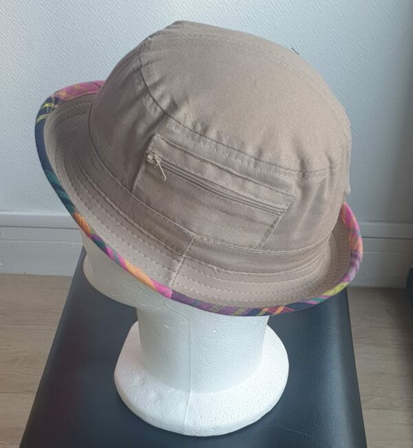 6.5Bob en marron clair sur un tissu 100% coton.  L'ajout de deux poches latérales zipées apporte une touche harmonieuse à ce couvre-chef. Les finitions en bordure sont en Madras et entièrement conçues puis réalisées aux ateliers AnjeroCréation à Paris.