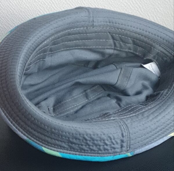 7.5Bob gris clair sur un tissu 100% coton. L'ajout de deux poches latérales zipées apporte une touche harmonieuse à ce couvre-chef. Les finitions en bordure sont en Madras et entièrement conçues puis réalisées aux ateliers AnjeroCréation à Paris.