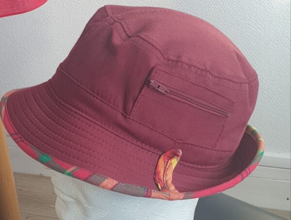 9.4Bob en rouge grenat sur un tissu 100% coton. L'ajout de deux poches latérales zipées apporte une touche harmonieuse à ce couvre-chef. Les finitions en bordure sont en Madras et entièrement conçues puis réalisées aux ateliers AnjeroCréation à Paris.