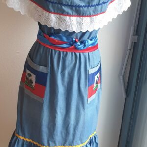 12.1Robe carabela en bleu clair sur une tenue traditionnelle haïtienne. Son élégance est mise en valeur par le tissage d'un col bardot en dentelles anglaises ainsi que par deux poches latérales symétriques . Des zigzags multicolors sur le haut et le bas de robe ajoutent à l'harmonie du vêtement doux et agréable à porter. Taille : XL. Entièrement confectionnée aux ateliers AnjéroCréation à Paris. Prix : 179.95€. 
