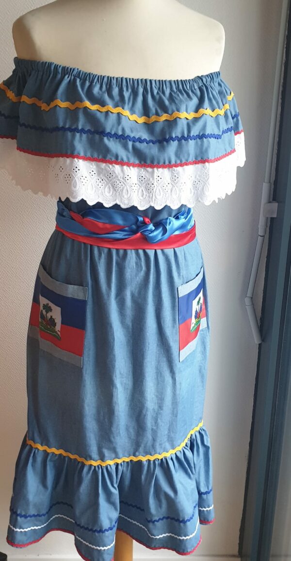 12.3Robe carabela en bleu clair sur une tenue traditionnelle haïtienne. Son élégance est mise en valeur par le tissage d'un col bardot en dentelles anglaises ainsi que par deux poches latérales symétriques . Des zigzags multicolors sur le haut et le bas de robe ajoutent à l'harmonie du vêtement doux et agréable à porter. Taille : XL. Entièrement confectionnée aux ateliers AnjéroCréation à Paris. 
