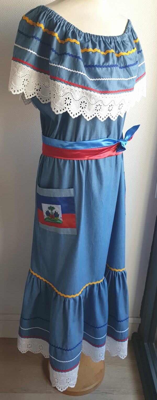 12.4Robe carabela en bleu clair sur une tenue traditionnelle haïtienne. Son élégance est mise en valeur par le tissage d'un col bardot en dentelles anglaises ainsi que par deux poches latérales symétriques . Des zigzags multicolors sur le haut et le bas de robe ajoutent à l'harmonie du vêtement doux et agréable à porter. Taille : XL. Entièrement confectionnée aux ateliers AnjéroCréation à Paris. 