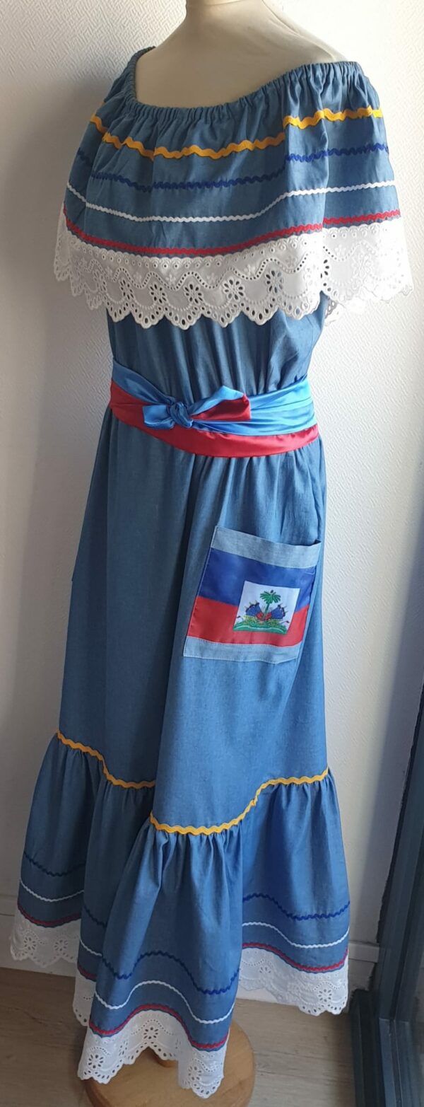 13.1Robe carabela longue en bleu sur une tenue traditionnelle. Le col bardot et le bas de robe sont brodés en dentelles animées. Les Zigzags sur le haut et le bas de robe sont respectivement jaunes, bleus foncé, blancs et rouges. Deux poches latérales rouges et bleues royales ornées du drapeau, ajoutent à l'harmonie du vêtement élastique à la partie rétrécie et 100% coton. Deux ceintures ont été pensées chacune d'entre elles en coureur unique, nouées à la taille. Entièrement confectionnée aux ateliers AnjéroCréation à Paris. Taille : XL, XXL. Prix : 259.95€. 