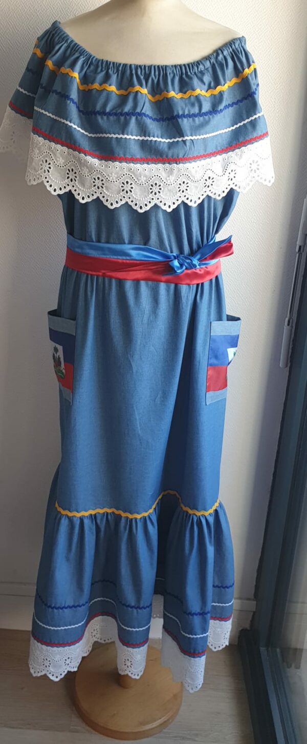 13.2Robe carabela longue en bleu sur une tenue traditionnelle. Le col bardot et le bas de robe sont brodés en dentelles animées. Les Zigzags sur le haut et le bas de robe sont respectivement jaunes, bleus foncé, blancs et rouges. Deux poches latérales rouges et bleues royales ornées du drapeau, ajoutent à l'harmonie du vêtement élastique à la partie rétrécie et 100% coton. Deux ceintures ont été pensées chacune d'entre elles en coureur unique, nouées à la taille. Entièrement confectionnée aux ateliers AnjéroCréation à Paris. Prix : 259.95€. 