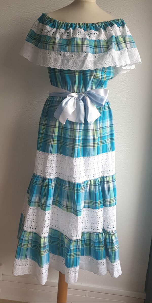1.1Robe madras sur une couleur bleue turquoise cent pour cent coton. Dentelles et broderies anglaises ainsi que le col bardot sont autant de spécificités affirmant le caractère de la robe. Elle est de plus élastique à la taille conférant ainsi une entière liberté d'adaptabilité. Une ceinture en satin bicolore ajoute à sa valeur. Taille : S, M, L, XL. Prix : 199,95€. Ce produit est entièrement confectionné dans les ateliers AnjeroCréation à Paris.