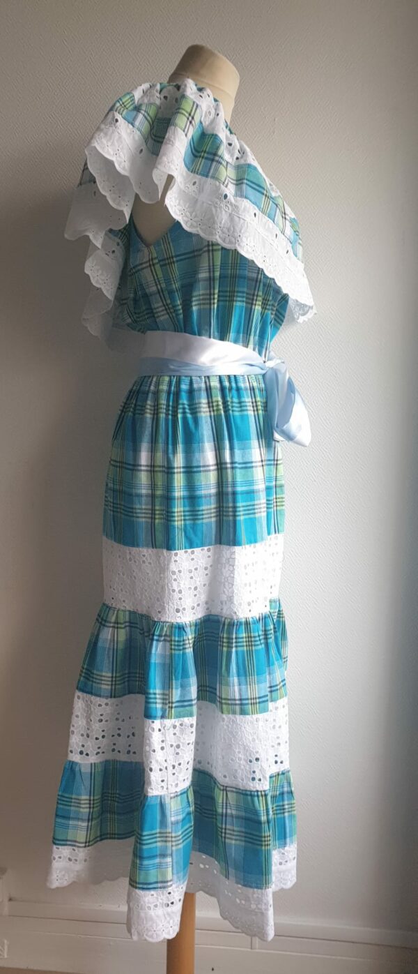 1.3Robe madras sur une couleur bleue turquoise cent pour cent coton. Dentelles et broderies anglaises ainsi que le col bardot sont autant de spécificités affirmant le caractère de la robe. Elle est de plus élastique à la taille conférant ainsi une entière liberté d'adaptabilité. Une ceinture en satin bicolore ajoute à sa valeur. Taille : S, M, L, XL.  Ce produit est entièrement confectionné dans les ateliers AnjeroCréation à Paris.
